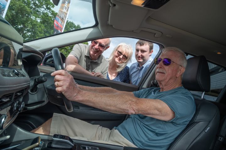 Interior view of a Nissan vehicle as a person sits in the driver’s seat while others look into the cabin