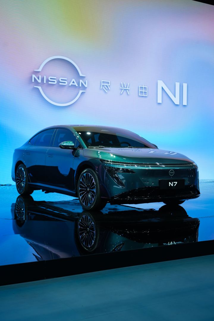 東風日産の緑色の新型セダン電気自動車「N7」。背景にパステルカラーの電子サインと日産ロゴ。