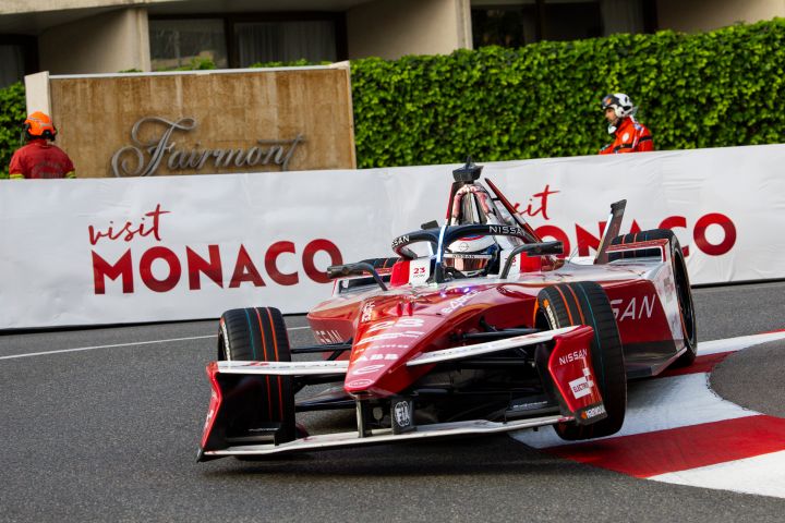 Oliver Rowland im Auto mit der Nummer 23 fährt in eine Kurve, im Hintergrund sind Schilder mit der Aufschrift „Visit Monaco“ zu sehen.