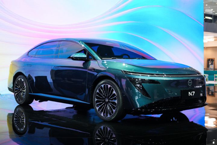 東風日産の緑色の新型セダン電気自動車「N7」。背景に渦巻き模様、パステルカラーの電子サインが見える。