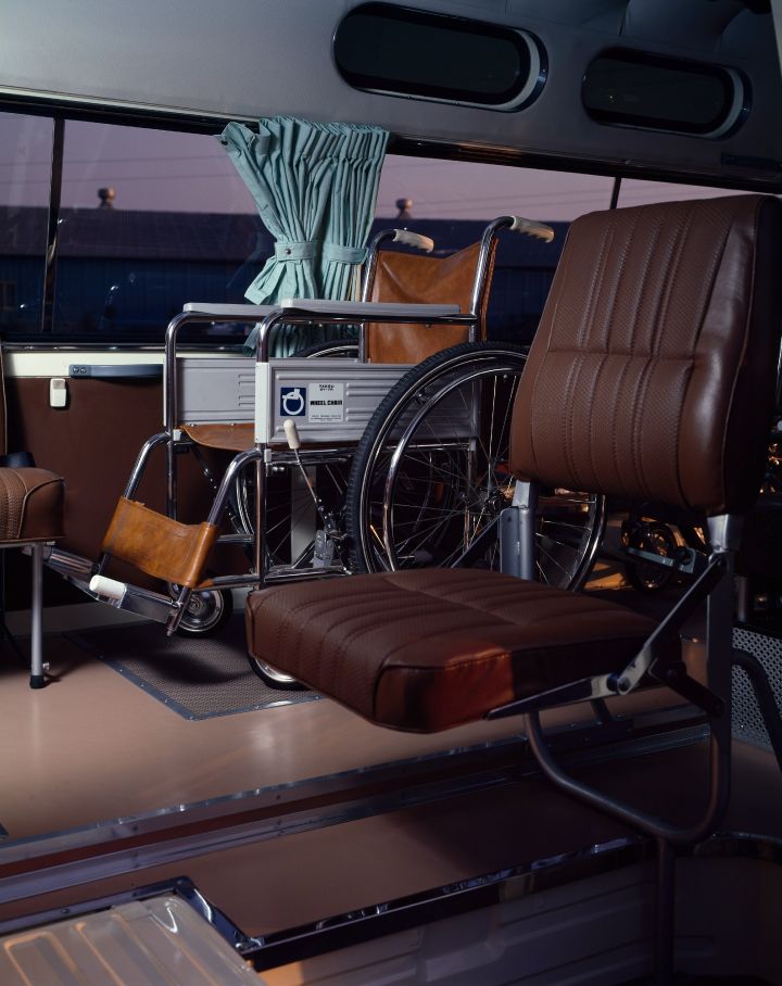 Interior of a vehicle adapted for wheelchair accessibility, featuring seating with brown upholstery, a secured wheelchair, and safety equipment.