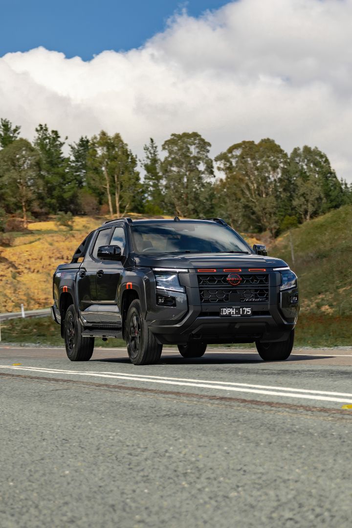 2026 Nissan Navara PRO-4X finished in Boulder Grey presented in a portrait-oriented front-quarter roadside view with dark wheels and dramatic sky.