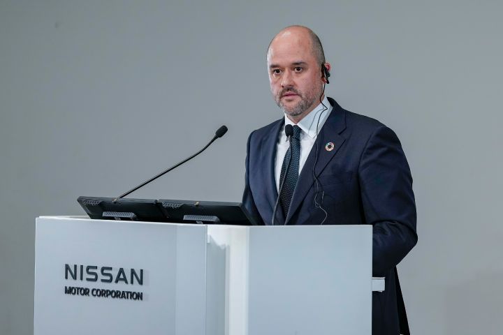 スーツとネクタイを着用し、SDGsのピンバッジを付けた日産自動車CEO イヴァン エスピノーサが、マイクが設置された演台でスピーチを行っている。