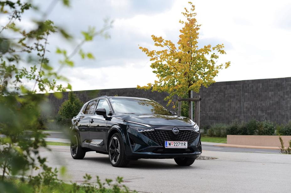 3/4 Frontansicht eines dunkelgrünen Nissan Qashqai, der auf einem baumbestandenen Parkplatz parkt