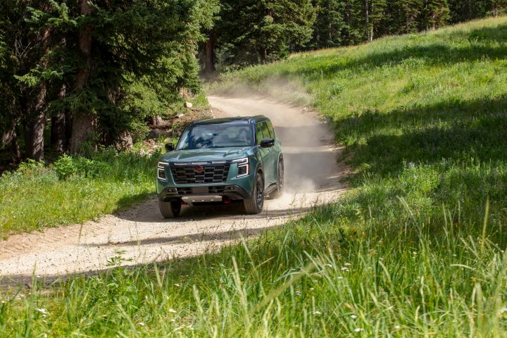 A dark green 2025 Nissan Armada Pro 4X barreling down a dirt path in the woods with dust flying up behind it.