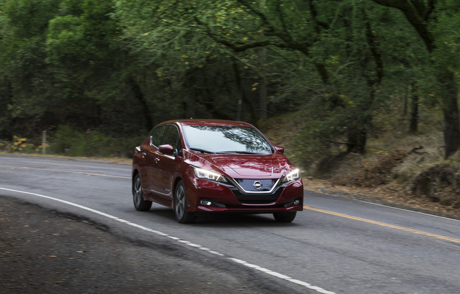 A Nissan LEAF driving down a road lined with trees