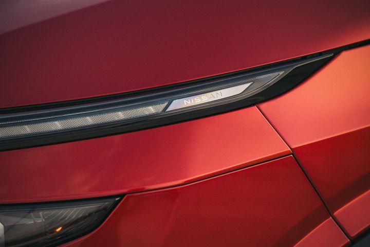 Detailansicht der Frontscheinwerfers mit Nissan Schriftzug des Nissan Qashqai in Fuji Sunset Red