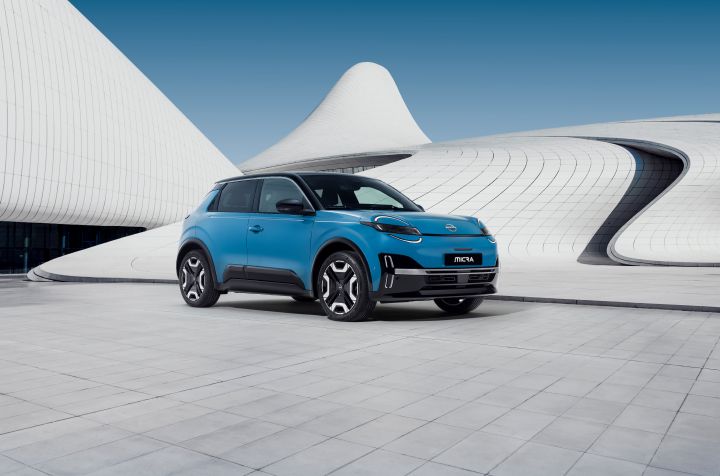 Ein neuer Nissan Micra in Blau steht vor einem modernen weißen Gebäude mit geschwungenen Architekturlinien