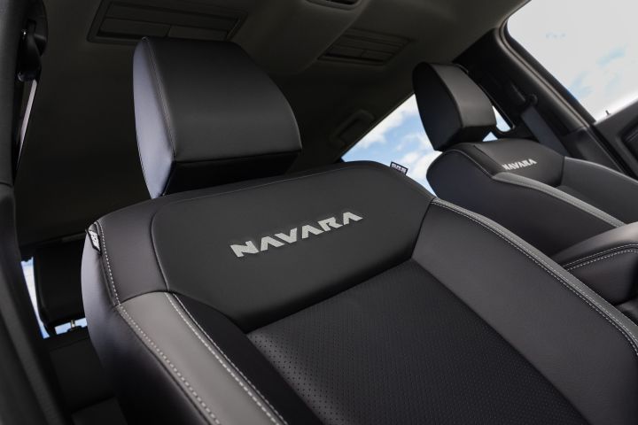 Low-angle view of the two front seats in a 2026 Nissan Navara ST-X, showing black upholstery, contrast stitching, and NAVARA embroidery on both seat backrests.