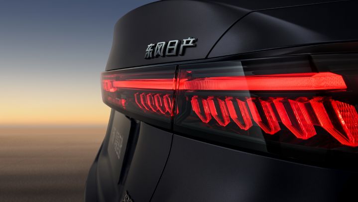 Close-up of the rear view of a black Teana, featuring bright red LED tail lights and the “Dongfeng Nissan” logo on the body. The background shows a sunset sky with soft light reflecting on the car.