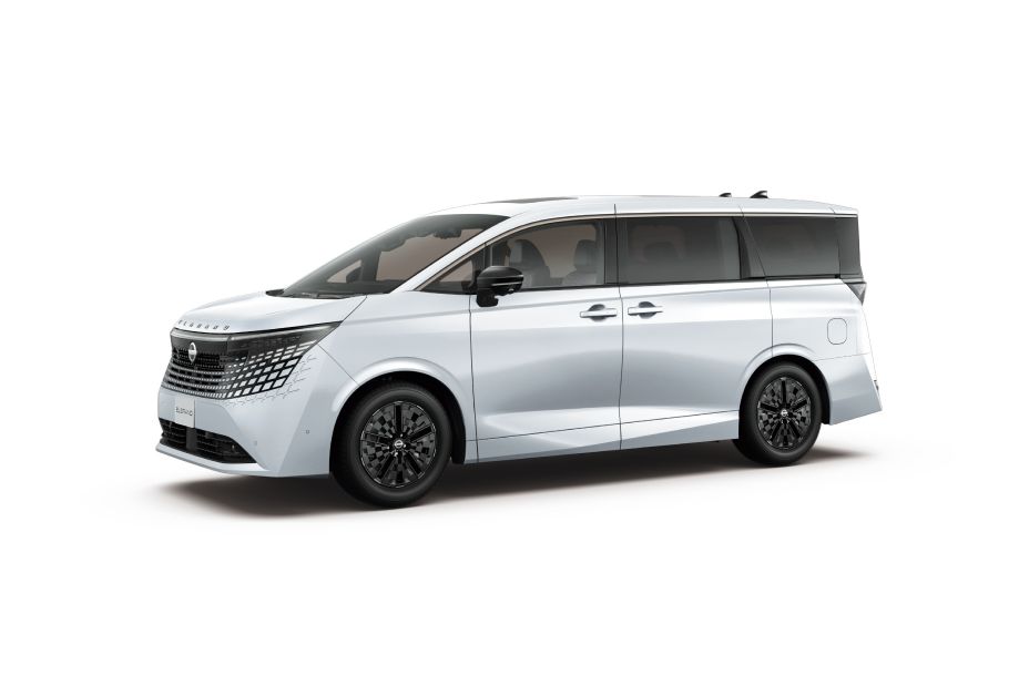 Studio image of the All-new ELGRAND in a white body color, shown from a front three-quarter view facing left. The vehicle features a black roof and dark pillars that create a sleek, continuous side profile. The front end is characterized by a large patterned grille and slim, sharp headlamps, while black alloy wheels add contrast to the overall design. The background is a plain light gray studio setting, highlighting the vehicle as the sole subject of the image.