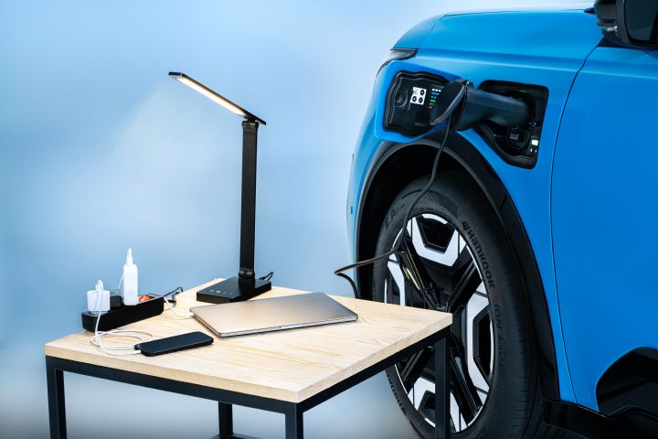 focused shot of micra's charging port with V2L Connected to an extension where a laptop, iPhone and lamp is charging on a coffee table