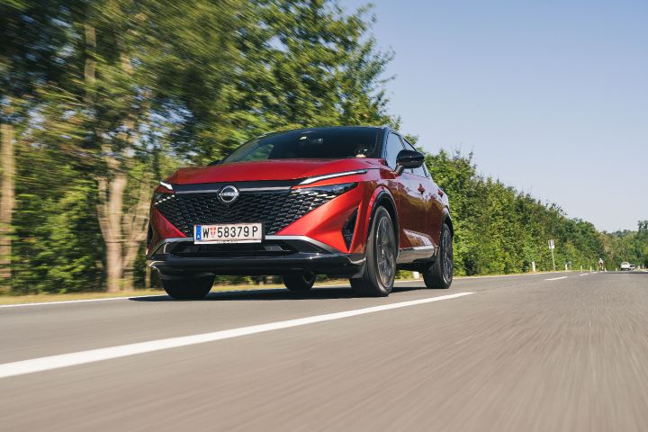 Fahraufnahme eines Nissan Qashqai in Fuji Sunset Red von vorne unten auf einer Landstraße mit Bäumen im Hintergrund