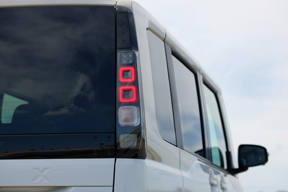 The new Nissan Roox kei car, in white, is shown from the rear with the right tail light illuminated.
