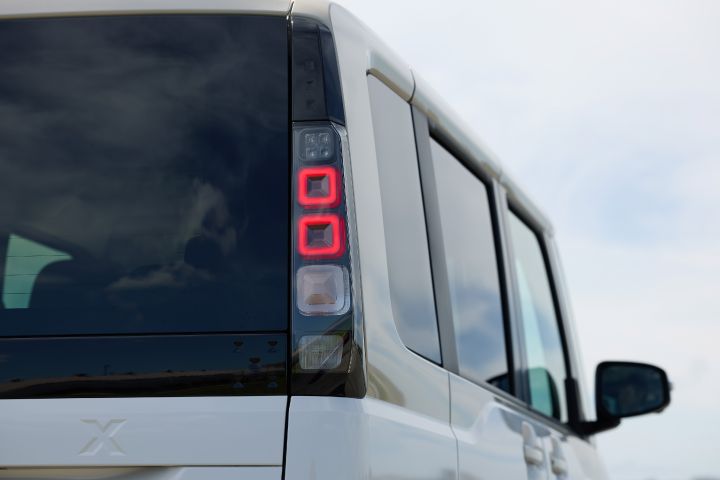 The new Nissan Roox kei car, in white, is shown from the rear with the right tail light illuminated.