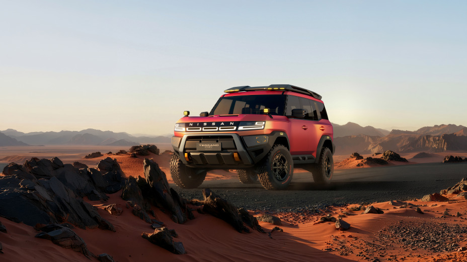 A red Terrano PHEV Concept driving at a front three-quarter angle across a rugged desert landscape. Rocks and sand appear in the foreground, with a sunset sky and distant mountains in the background.
