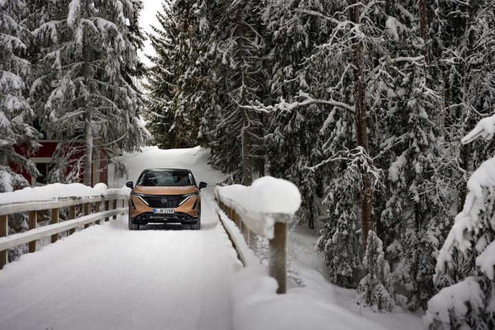 The Ariya e‑4ORCE driving on a snow-covered wooden bridge with trees in the background