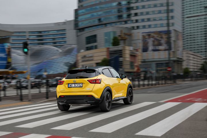 Jadący żółty Nissan Juke (widok z tyłu) z budynkami w tle