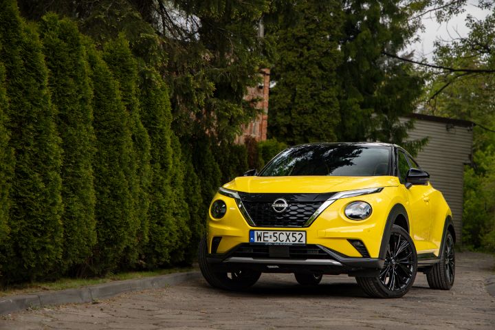 Żółty Nissan Juke stojący bokiem na tle budynku i drzew