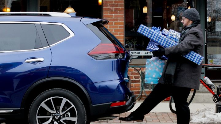 A man is carrying presents while opening the back of a 2019 Nissan Rogue.
