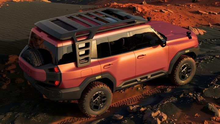A red Terrano PHEV Concept seen from a rear three-quarter view, driving to the left across a desert landscape at sunset. Rolling sand dunes and rocky hills stretch into the background, lit by soft evening light.