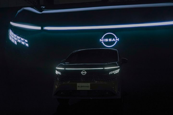In a dark setting, the all-new Elgrand is positioned facing forward. Behind it, a large illuminated screen displays glowing lines and the Nissan logo, creating a futuristic atmosphere.