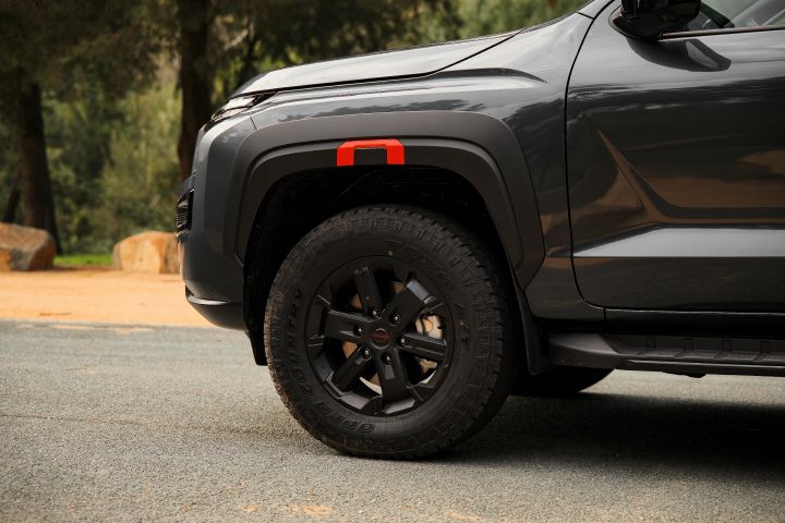 2026 Nissan Navara PRO-4X finished in Boulder Grey showing the front-side wheel, chunky tyre and red-highlighted fender flare above black cladding.