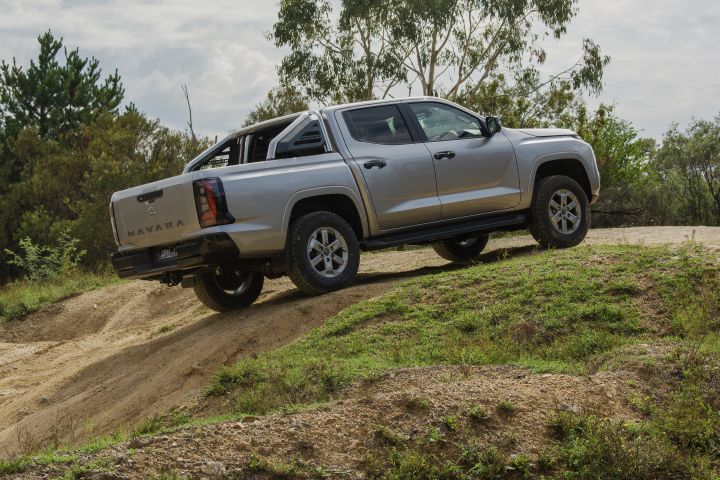 2026 Nissan Navara ST dual cab ute finished in Summit Silver displayed from the rear three-quarter angle on a grassy off-road rise.