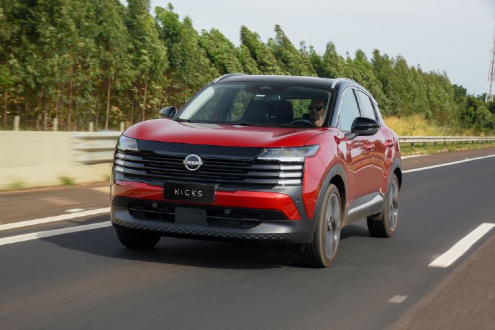 SUV Nissan Kicks vermelho em movimento em uma estrada, com céu limpo e árvores ao fundo