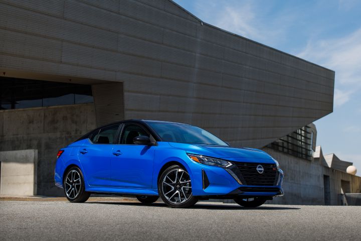Front right ¾ view of a blue 2024 Nissan Sentra parked in front of a geometrical building.