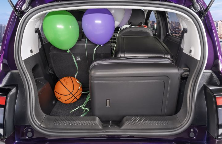 Photograph showing open trunk of a purple vehicle, demonstrating cargo space with green, purple, and white balloons plus an orange basketball. Black rear seats, gray interior trim, cargo floor, and city scenery appear in background.