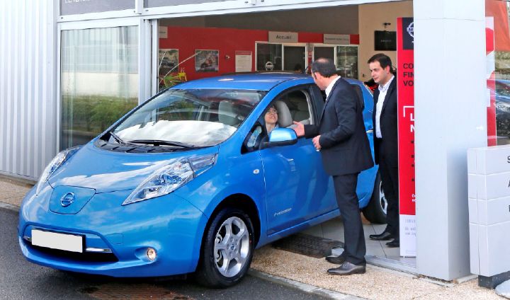 a woman driving off in a blue Nissan LEAF
