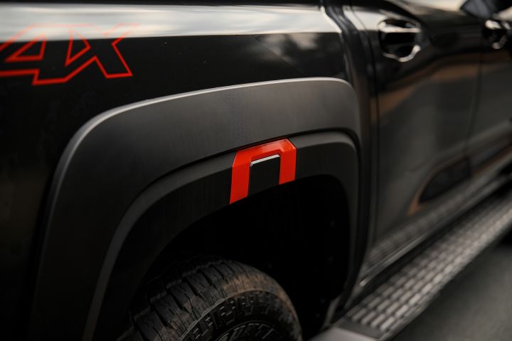 2026 Nissan Navara PRO-4X finished in Boulder Grey showing the rear wheel arch with red-accented fender flare, side step, tyre edge and partial 4X decal.