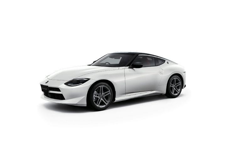 White Fairlady Z photographed in a light gray studio setting. The vehicle is shown from a front-left three-quarter angle, with the front end facing toward the left side of the image. The coupe features a two-tone exterior with a white body and black roof, highlighting its sharp headlights and classic long-hood, short-deck proportions. Silver alloy wheels complement the design, while the clean studio background emphasizes the car’s sporty styling and sculpted body lines.