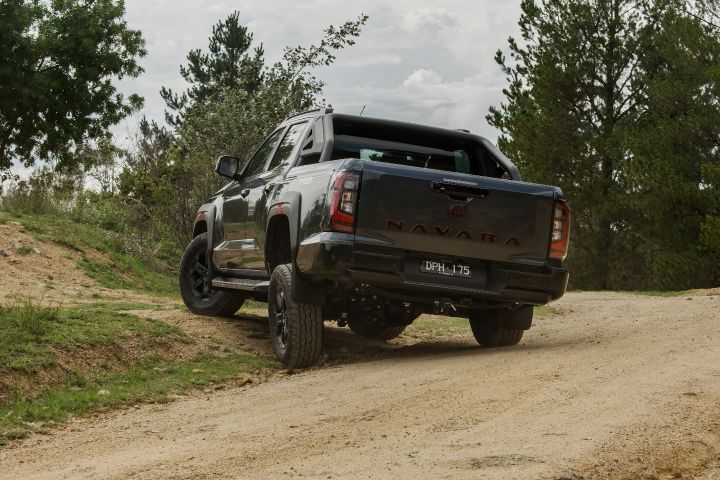 2026 Nissan Navara PRO-4X finished in Boulder Grey shown rear three‑quarter on compacted dirt with NAVARA tailgate embossing, towbar and vertical tail‑lamps.