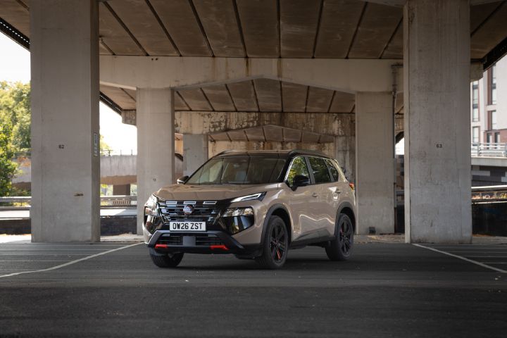 Statische 3/4 Frontansicht eines hellbraunen Nissan X‑Trail der unter fast gleichfarbigen Brückenpfeilern steht