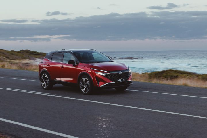 Un Nissan Qashqai rouge roule sur une route asphaltée en bord de mer.