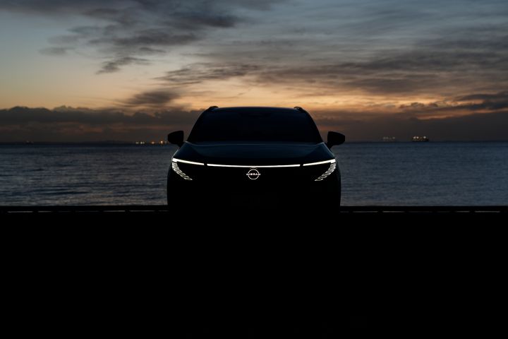 Frontale Silhouette eines Nissan LEAF bei Dunkelheit, die LED Scheinwerfer und das Nissan Logo leuchten