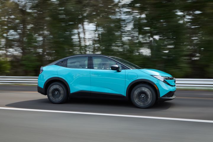 Right profile view of the 2026 Nissan LEAF driving along a tree-lines highway, the background is blurred due to speed.