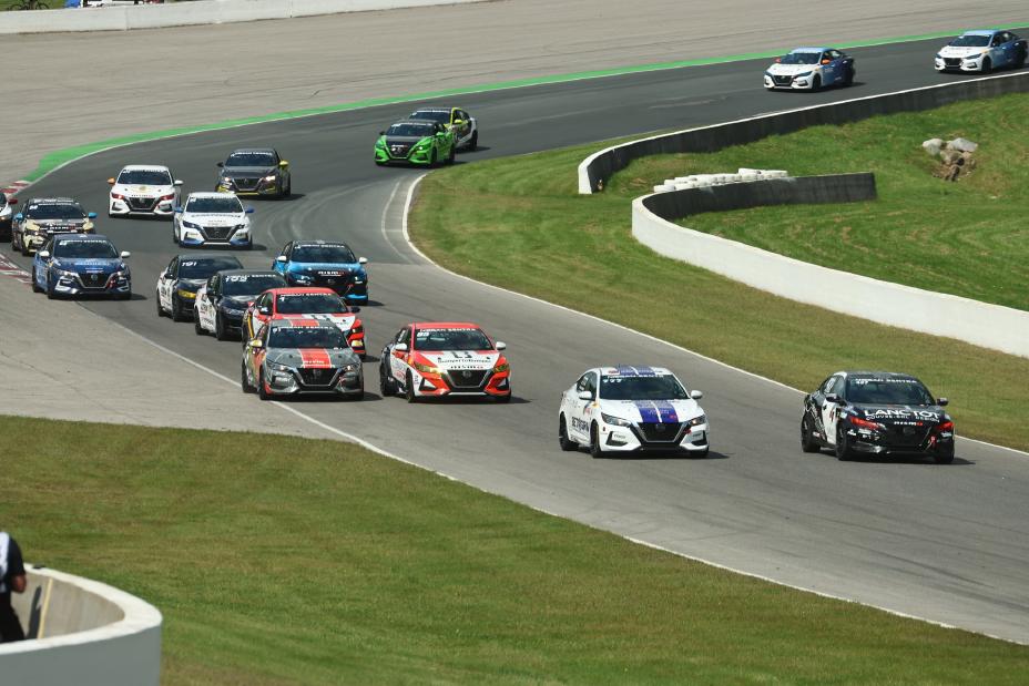 Various Nissan Sentra race cars driving around the bend of a race track with green grass on either side of the track