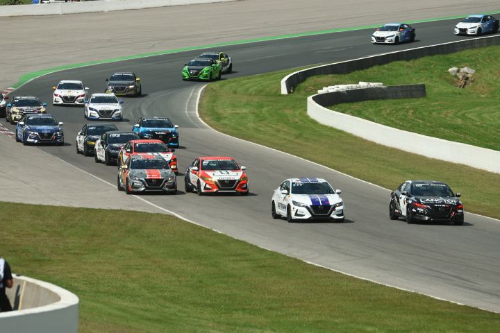Various Nissan Sentra race cars driving around the bend of a race track with green grass on either side of the track