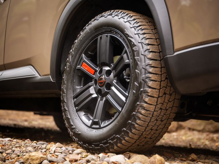 Close up of the wheel and tire on a 2025 Nissan Rogue rock creek, the Nissan emblem and one spoke are red.