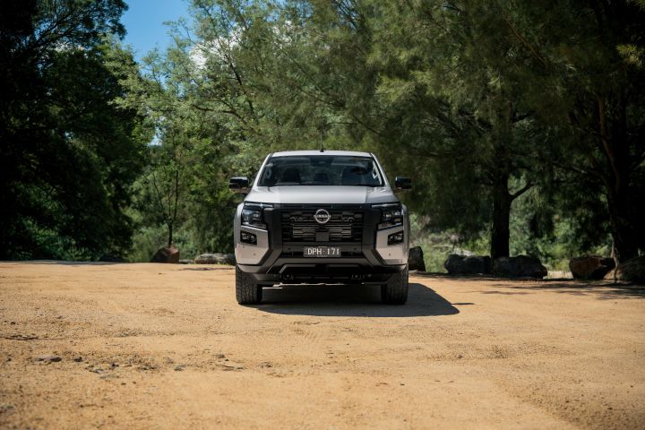 2026 Nissan Navara ST dual cab ute finished in Summit Silver presented in a wide front view on gravel, emphasizing the broad grille and balanced stance.