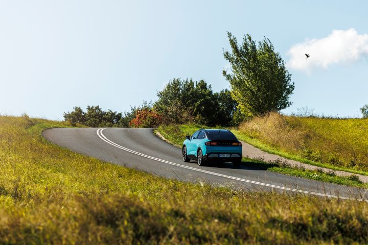 Dänische Landstraße mit grünen Büschen und Feldern zu beiden Seiten der Fahrbahn, auf der mittig klein ein türkiser Nissan LEAF zu sehen ist