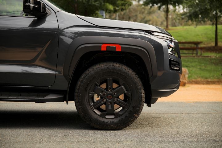 2026 Nissan Navara PRO-4X finished in Boulder Grey showing the front wheel area with matt black alloy, tyre and red-accented fender flare.
