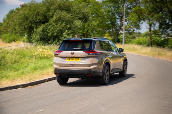 Nissan X‑Trail driving along a country road, shown from the rear, with a forest in the background.