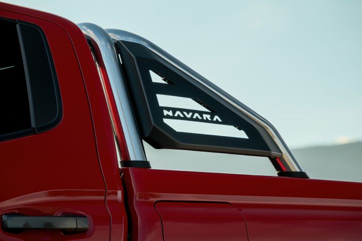 Close-up side detail of a 2026 Nissan Navara ST‑X in Outback Red, showing the chrome sports bar, rear cabin section, and tray-side panel with the NAVARA insert visible.