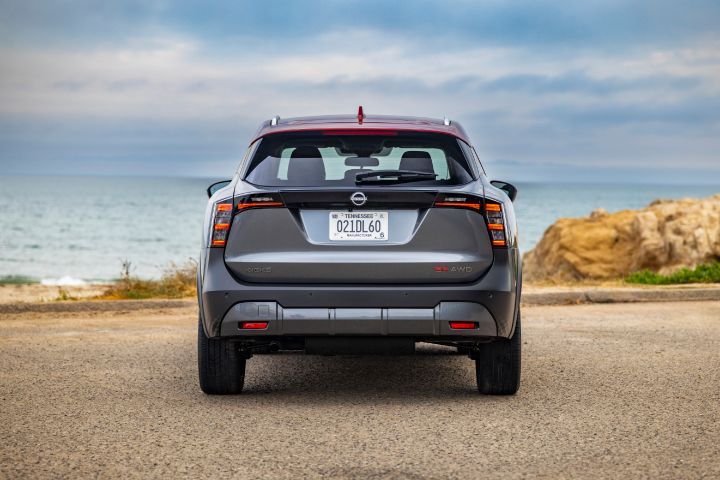 Rear view of a silver 2025 Nissan Kicks parked on a gravel lot overlooking the ocean on a cloudy day.