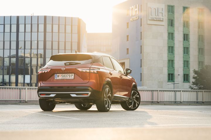 Heckansicht eines Nissan Qashqai in Fuji Sunset Red auf einem Parkplatz vor einem Hotelgebäude