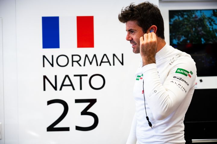 Norman Nato in seinem weißen T-Shirt steckt sich gerade seinen Ohrhörer ein, während er neben seinem Namen, seiner Startnummer und seiner Flagge an der Wand der Teamgarage steht.